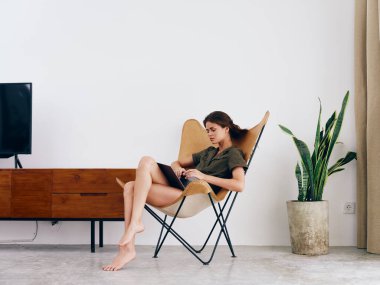 Bayan öğrenci çalışması, evinde dizüstü bilgisayarı olan bir sandalyede oturuyor. Gülümse ve rahatla, modern stil İskandinav yaşam tarzı, kopyalama alanı. Yüksek kalite fotoğraf