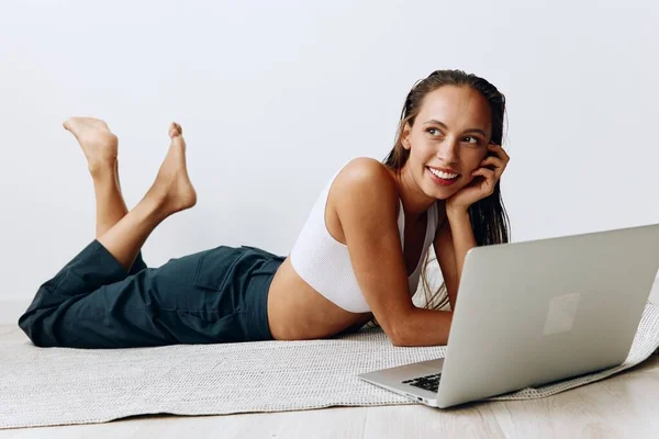 A woman lies on the floor at home and smiles with her teeth while looking at a laptop while chatting online and watching TV shows on her day off. High quality photo