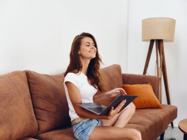 Kanepede oturan serbest çalışan bir kadın güzel bir dizüstü bilgisayarla gülümsüyor, modern stil bir İskandinav yaşam tarzı, kopyalama alanı. Yüksek kalite fotoğraf