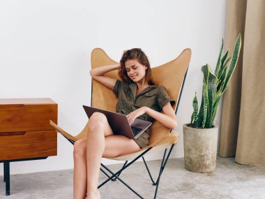 Sandalyesinde oturan serbest çalışan bir kadın öğrenci evinde dizüstü bilgisayarla çalışıyor gülümse ve rahatla, modern stil İskandinav yaşam tarzı, kopyalama alanı. Yüksek kalite fotoğraf