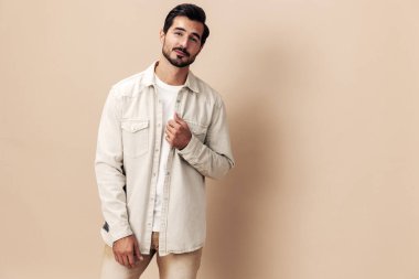 Beyaz tişörtlü bej bir arka planda poz veren şık bir erkek gülümseme modeli kameraya bakıyor, modaya uygun giyim tarzı, fotokopi alanı, yazı için yer. Yüksek kalite fotoğraf