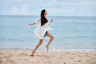 Spor kadın plaj boyunca sarı bir atlet ve kot şortla kumsalda koşuyor. Uçan saçlar, deniz manzarası, plaj tatili ve seyahat. Yüksek kalite fotoğraf