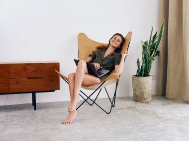 Kız öğrenci eğitimi, evinde dizüstü bilgisayarı olan bir sandalyede oturuyor gülümse ve rahatla, modern İskandinav tarzı iç mimari yaşam tarzı, kopyalama alanı. Yüksek kalite fotoğraf