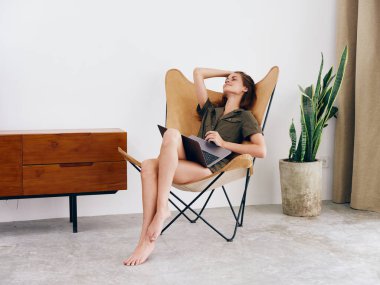 Kız öğrenci eğitimi, evinde dizüstü bilgisayarı olan bir sandalyede oturuyor gülümse ve rahatla, modern İskandinav tarzı iç mimari yaşam tarzı, kopyalama alanı. Yüksek kalite fotoğraf