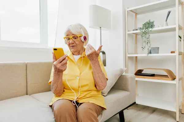 Happy elderly woman looking into phone video call smile, technology for communication, bright modern interior, lifestyle online communication. High quality photo