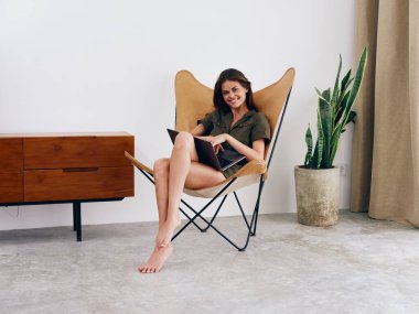 Kız öğrenci eğitimi, evinde dizüstü bilgisayarı olan bir sandalyede oturuyor gülümse ve rahatla, modern İskandinav tarzı iç mimari yaşam tarzı, kopyalama alanı. Yüksek kalite fotoğraf