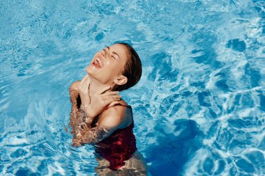 Kırmızı mayo içinde yüzen, uzun saçlı, güneş kremli cilt koruması olan, tatilde rahatlama konsepti olan mutlu bir kadın. Yüksek kalite fotoğraf