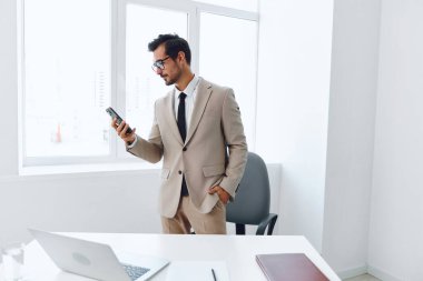 Genç adam yaşam tarzı sohbet ofisi dizüstü bilgisayarı modern iş adamı telefon video işi bilgisayar gülümsemesi akıllı telefon çekici iş yeri teknolojisi mobil beyaz takım elbise