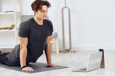 Aktivite adamı genç insan sağlıklı fiziksel aktif ev içi egzersiz odası çevrimiçi yaşam eğitimi ev germe dizüstü bilgisayar fitness saati uyumu