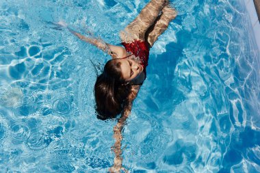 Havuzda kırmızı mayo giyen, suda yatan ve mavi havuzda yüzen güzel bir gülümsemesi olan genç bir kadın. Tatilde dinlenme kavramı. Yüksek kalite fotoğraf