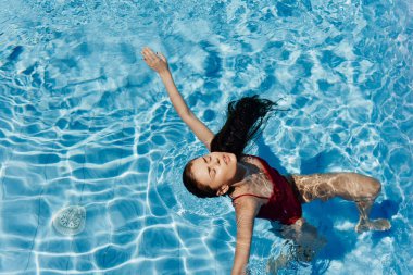Havuzda kırmızı mayo giyen, suda yatan ve mavi havuzda yüzen güzel bir gülümsemesi olan genç bir kadın. Tatilde dinlenme kavramı. Yüksek kalite fotoğraf