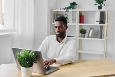 Adam dizüstü bilgisayarda gülümseyen siber uzay ofis öğrencisi işi. Kapalı mekanda serbest çalışan, internetten internete bakan internet işadamı görünümlü, web işadamı masasında oturan Afrikalı Amerikan kopya bilgisayarlı sohbet programı eğitimi.