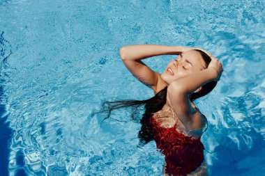 Kırmızı mayo içinde yüzen, uzun saçlı, güneş kremli cilt koruması olan, tatilde rahatlama konsepti olan mutlu bir kadın. Yüksek kalite fotoğraf
