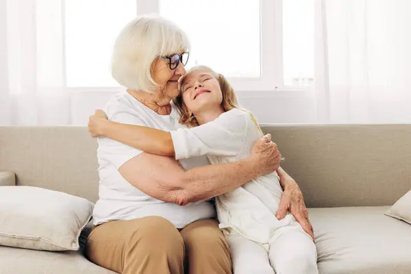 Woman hug generation elderly senior child home indoor mother couch grandchild girl grandmother old lifestyle sitting happy love sofa granddaughter daughter family