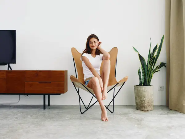 坐在皮革扶手椅上的女人笑着带着牙齿生活方式 悠闲地呆在家里 用白色的墙壁装饰着时髦的现代室内装饰 复制空间 高质量的照片 — 图库照片