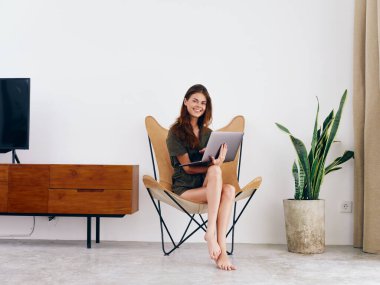 Bayan öğrenci çalışması, evinde dizüstü bilgisayarı olan bir sandalyede oturuyor. Gülümse ve rahatla, modern stil İskandinav yaşam tarzı, kopyalama alanı. Yüksek kalite fotoğraf