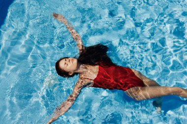 Havuzda yüzen kırmızı mayo giymiş, suda uzanan ve havuzda yüzen güzel bir gülümsemesi olan genç bir kadın. Tatilde dinlenme kavramı. Yüksek kalite fotoğraf