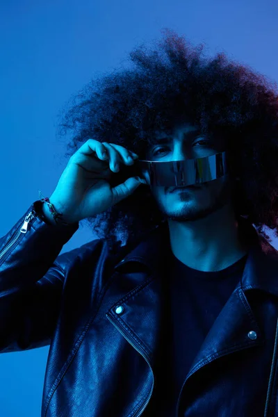 ブルーバックグラウンドのスタイリッシュなメガネとカーリーヘアのファッション男性の肖像画 多国籍 カラーライト ブラックレザージャケットのトレンド モダンなコンセプト 高品質の写真 — ストック写真