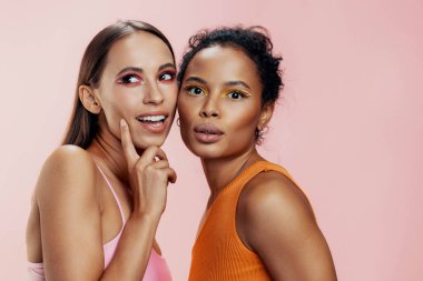 Makyajcı kadın, stüdyo ten rengiyle karışık pembe, mutlu, güzel bir portre, iki çekici yarış kızı, güzel Afro-Afrikalı, Amerikan vücut bakımını parlatıyor.