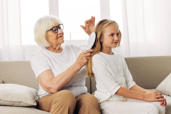 Lifestyle woman child elderly senior family girl mother hair generation hug old sofa grandmother sitting love happy hair combing couch comb granddaughter home daughter