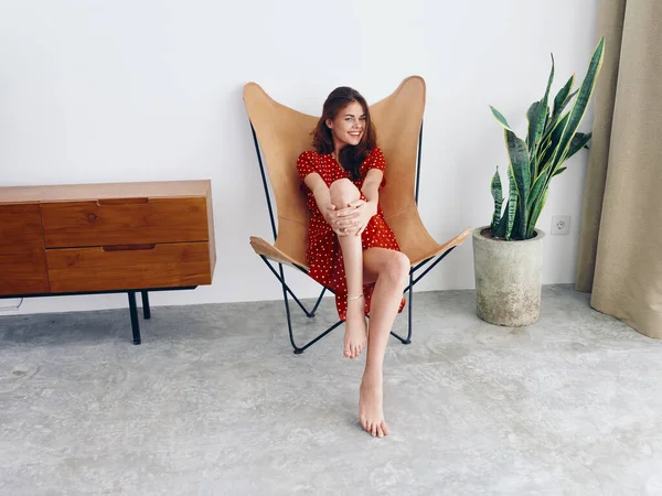 坐在皮革扶手椅上的女人带着牙齿微笑生活风格的红色波尔卡圆点裙 在家里穿着时尚的现代内饰 墙壁洁白 高质量的照片 — 图库照片