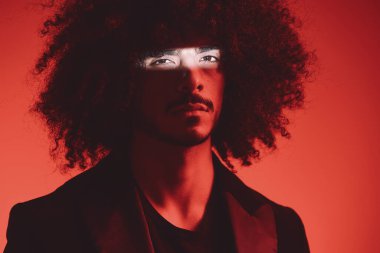 Kırmızı arka planda kıvırcık saçlı bir adamın moda portresi, çok uluslu, renkli ışık, modaya uygun, modern konsept. Yüksek kalite fotoğraf