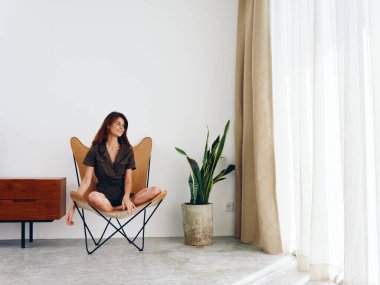 Pencerenin yanındaki deri koltukta oturan kadın gülümsüyor, modern İskandinav tarzı iç mekan, kopyalama alanı. Yüksek kalite fotoğraf