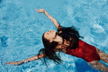 Kırmızı mayo içinde yüzen, uzun saçlı, güneş kremli cilt koruması olan, tatilde rahatlama konsepti olan mutlu bir kadın. Yüksek kalite fotoğraf