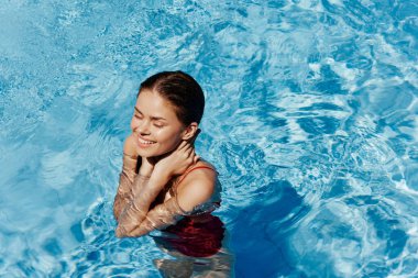 Kırmızı mayo içinde yüzen, uzun saçlı, güneş kremli cilt koruması olan, tatilde rahatlama konsepti olan mutlu bir kadın. Yüksek kalite fotoğraf