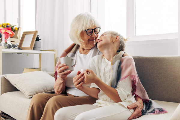 Woman home sofa happy mugs hug girl couch sitting plaid child hugging lifestyle mother family love winter old elderly grandmother senior granddaughter daughter