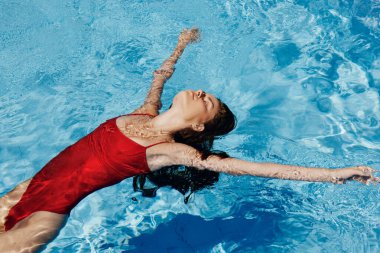 Kırmızı mayo içinde yüzen, uzun saçlı, güneş kremli cilt koruması olan, tatilde rahatlama konsepti olan mutlu bir kadın. Yüksek kalite fotoğraf