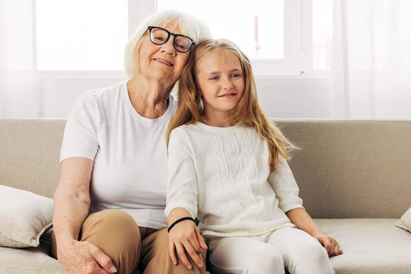 Woman child elderly grandmother hug granddaughter happy love senior generation family old girl daughter sofa mother sitting lifestyle home couch
