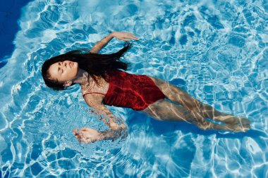 Havuzda kırmızı mayo giyen, suda yatan ve mavi havuzda yüzen güzel bir gülümsemesi olan genç bir kadın. Tatilde dinlenme kavramı. Yüksek kalite fotoğraf