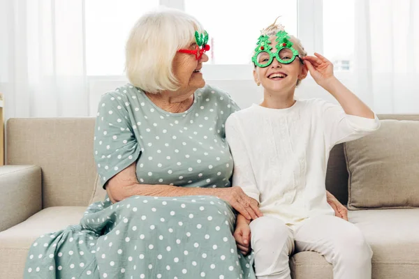 Grandparent woman smile grandmother happy child christmas couch sofa grandchild granddaughter home holiday family love gift cosy new together year glasses girl