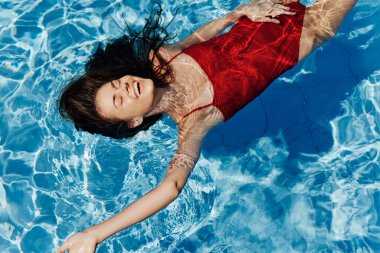 Havuzda yüzen kırmızı mayo giymiş, suda uzanan ve havuzda yüzen güzel bir gülümsemesi olan genç bir kadın. Tatilde dinlenme kavramı. Yüksek kalite fotoğraf
