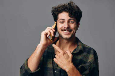 Genç, kendine güvenen, mavi, şık, telefon görünümlü, gri, siyah sakallı, arka planda bir adam. Stüdyo gülümsemesi.