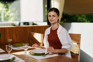 Güzel bir gülümseme ile yemek masasında oturan şık bir kadın, ev modern iç mekan, gün batımı ışığı, konfor içinde yaşam tarzı. Yüksek kalite fotoğraf