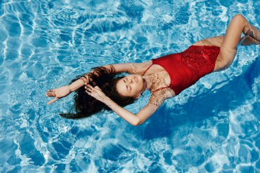 Havuzda kırmızı mayo giyen, suda yatan ve mavi havuzda yüzen güzel bir gülümsemesi olan genç bir kadın. Tatilde dinlenme kavramı. Yüksek kalite fotoğraf