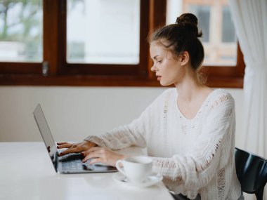 Evde rahat bir yerde, bir bardak içkiyle masa başında çalışan yaratıcı genç bir kadın. İnternette gülümsemesi, iletişimi ve eğitimi olan bir ofis çalışanı. Yüksek kalite fotoğraf
