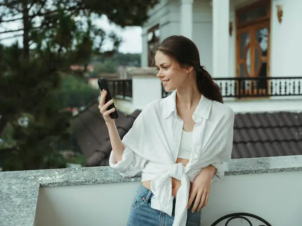Woman on the balcony of the house with phone beautiful smile on a day off, beautiful view of nature in the mountains, lifestyle vacation in the hotel. High quality photo