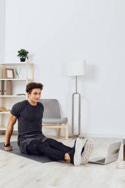 Adam evde sağlık aktivitesi eğitiyor ev yaşam tarzı kas evi sağlıklı insanı dizüstü bilgisayarla spor odası kas yogası egzersizi yapıyor.