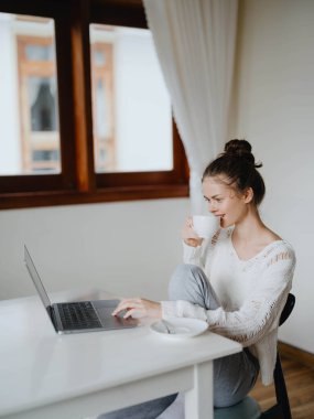 Evde rahat bir yerde, bir bardak içkiyle masa başında çalışan yaratıcı genç bir kadın. İnternette gülümsemesi, iletişimi ve eğitimi olan bir ofis çalışanı. Yüksek kalite fotoğraf