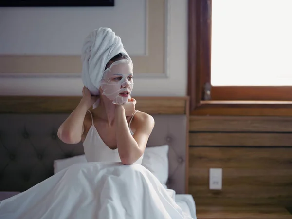 Młoda Kobieta Leżąca Łóżku Nawilżającą Maską Twarzy Białym Ręcznikiem Głowie — Zdjęcie stockowe