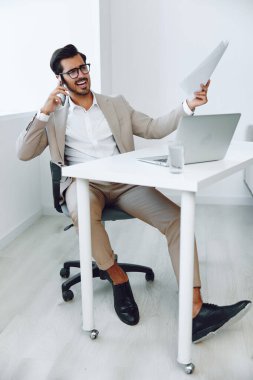 Telefoncu bürosundan konuşma kazananı laptop yaşam tarzı iş adamı gözlükleri gülümseme teknolojisi masa başı modern yönetici bej bilgisayar belgesi çekici takım elbise işi