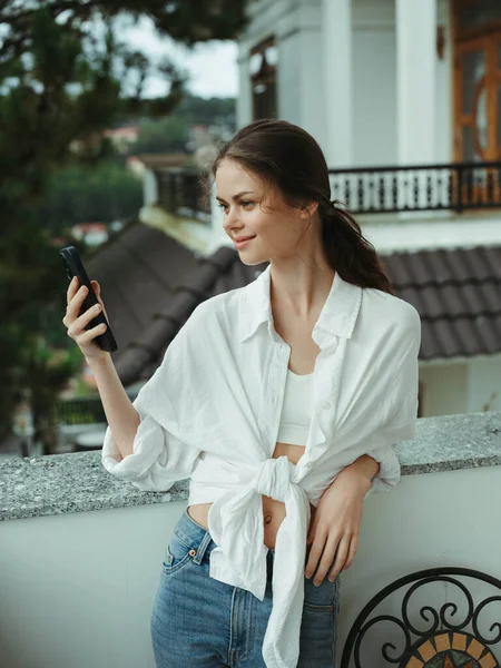 Woman on the balcony of the house with phone beautiful smile on a day off, beautiful view of nature in the mountains, lifestyle vacation in the hotel. High quality photo