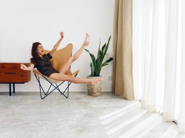 Pencere kenarında oturan bir kadın neşeli ayaklar ve eller yukarı, modern İskandinav tarzı iç mekan, kopyalama alanı. Yüksek kalite fotoğraf