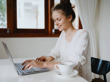 Evde rahat bir yerde, bir bardak içkiyle masa başında çalışan yaratıcı genç bir kadın. İnternette gülümsemesi, iletişimi ve eğitimi olan bir ofis çalışanı. Yüksek kalite fotoğraf