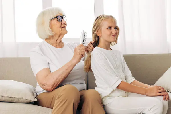 Woman sitting couch sofa old family senior child daughter mother hair hug home grandmother hair comb girl combing happy granddaughter generation lifestyle elderly love