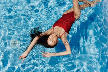 Havuzda kırmızı mayo giyen, suda yatan ve mavi havuzda yüzen güzel bir gülümsemesi olan genç bir kadın. Tatilde dinlenme kavramı. Yüksek kalite fotoğraf