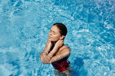 Kırmızı mayo içinde yüzen, uzun saçlı, güneş kremli cilt koruması olan, tatilde rahatlama konsepti olan mutlu bir kadın. Yüksek kalite fotoğraf